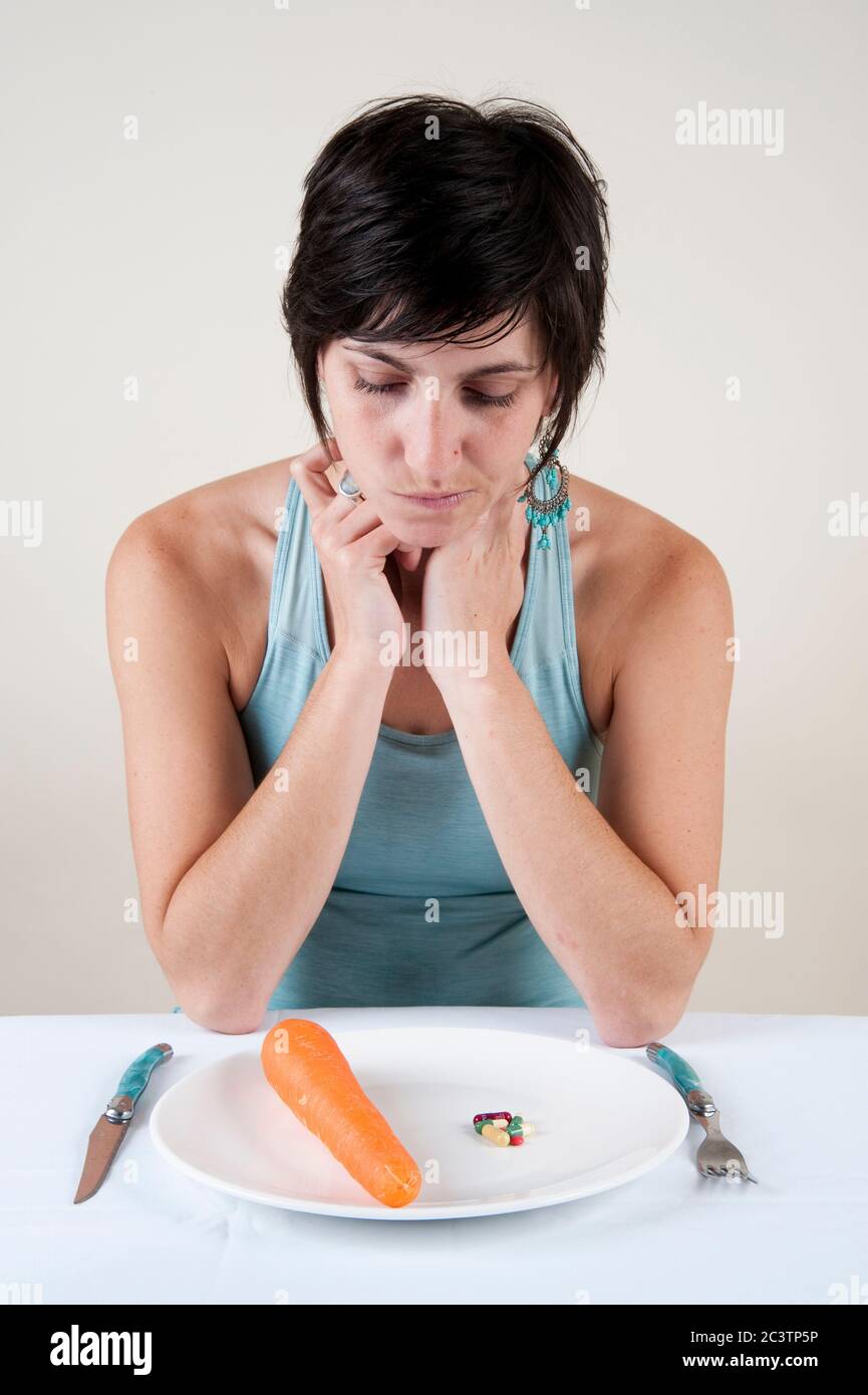 Mangiare disordine concetto - Studio shot di una affamata depressa e frustrata modello femminile nei suoi 20 con un piatto di verdure di fronte a lei su bianco Foto Stock