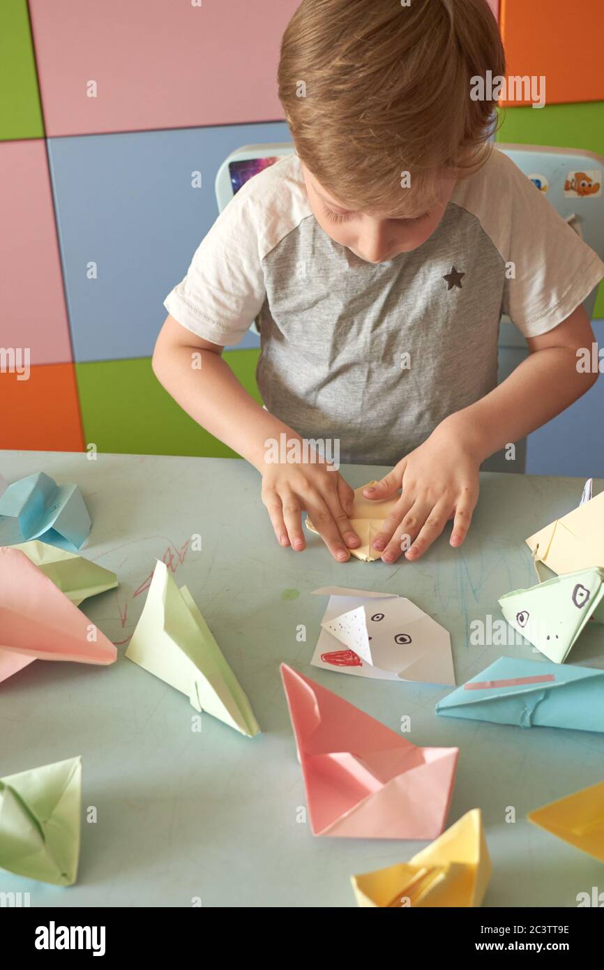 6 anni ragazzo fa un origami aerei e rane durante la quarantena Covid-19 Foto Stock