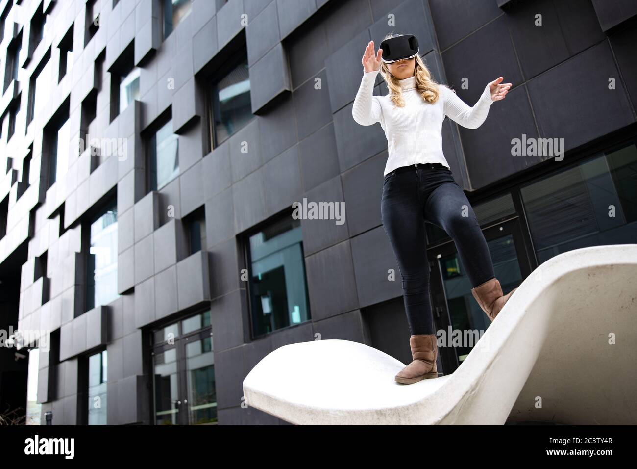 Donna bionda che indossa occhiali di realtà virtuale contro l'edificio futuristico Foto Stock
