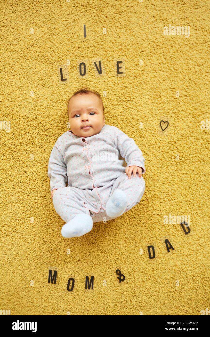 Vista dall'alto verticale sul simpatico bambino misto-razza sdraiato su soffice tappeto giallo con parole che amo mamma e papà Foto Stock
