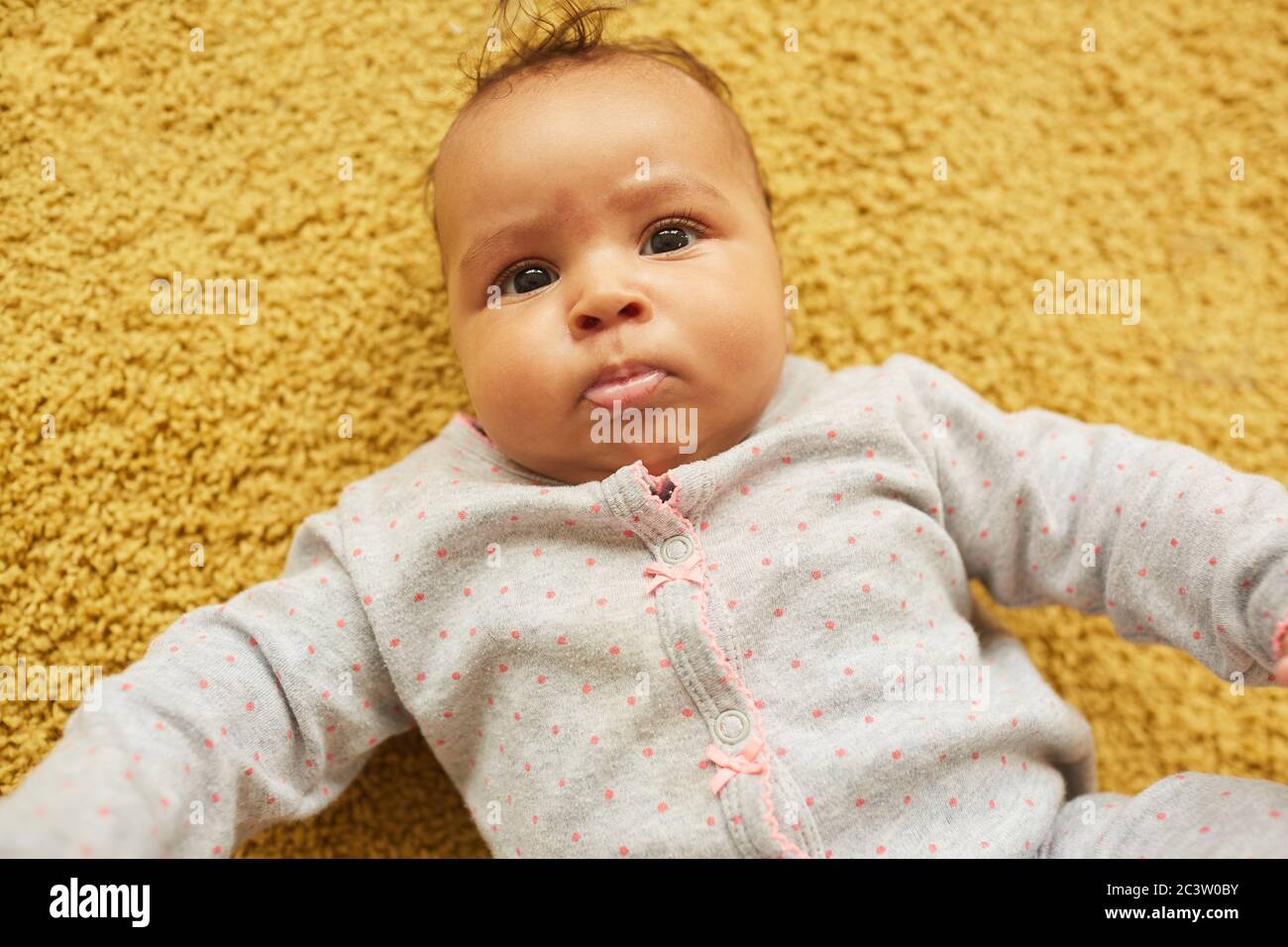Sopra il ritratto di cute misto-razza bambino guardando la macchina fotografica mentre si trova su morbido tappeto giallo, copia spazio Foto Stock