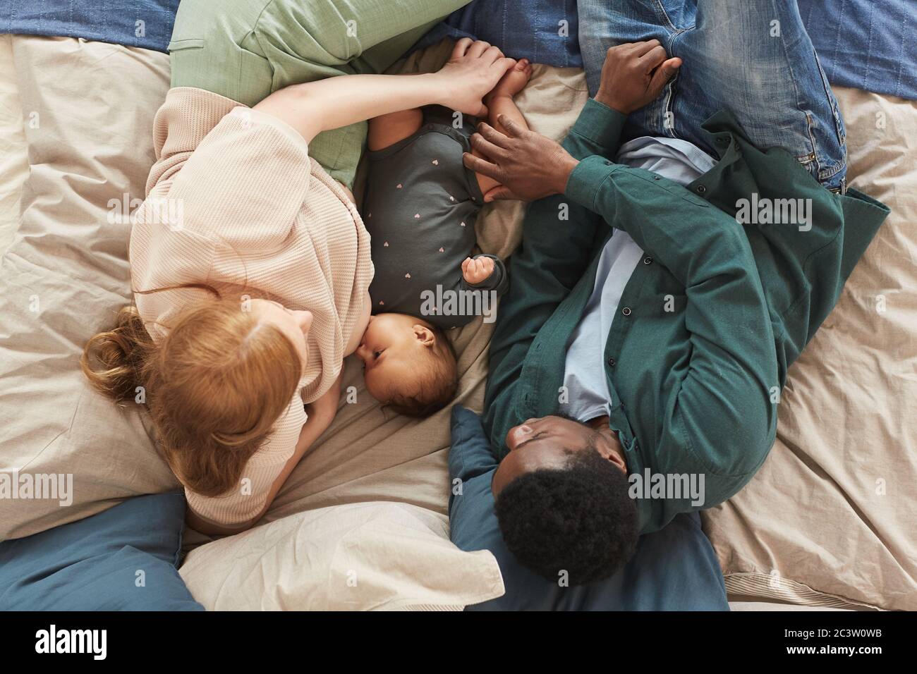 Sopra il ritratto della famiglia interracial con il bambino carino che si trova sul letto comodo a casa, spazio di copia Foto Stock