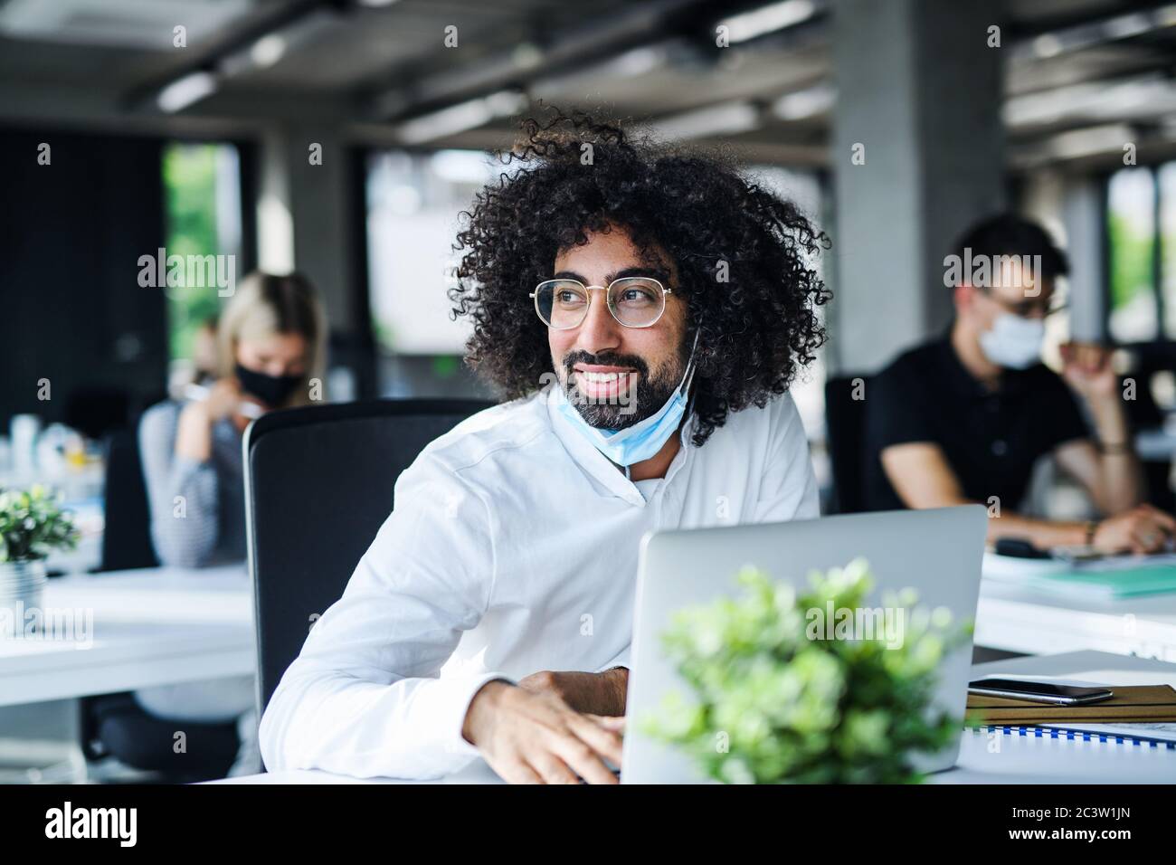 Ritratto di giovane uomo con maschera facciale di nuovo al lavoro in ufficio dopo il blocco. Foto Stock