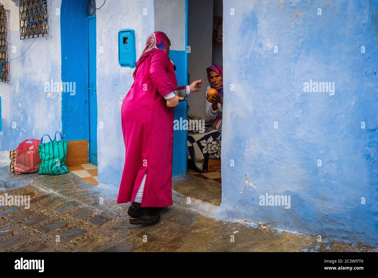 Marocco: Chefchaouen, la città blu. Atmosfera nella Città Vecchia: Donna in un vicolo della medina dando un arancio ad una vecchia donna Foto Stock