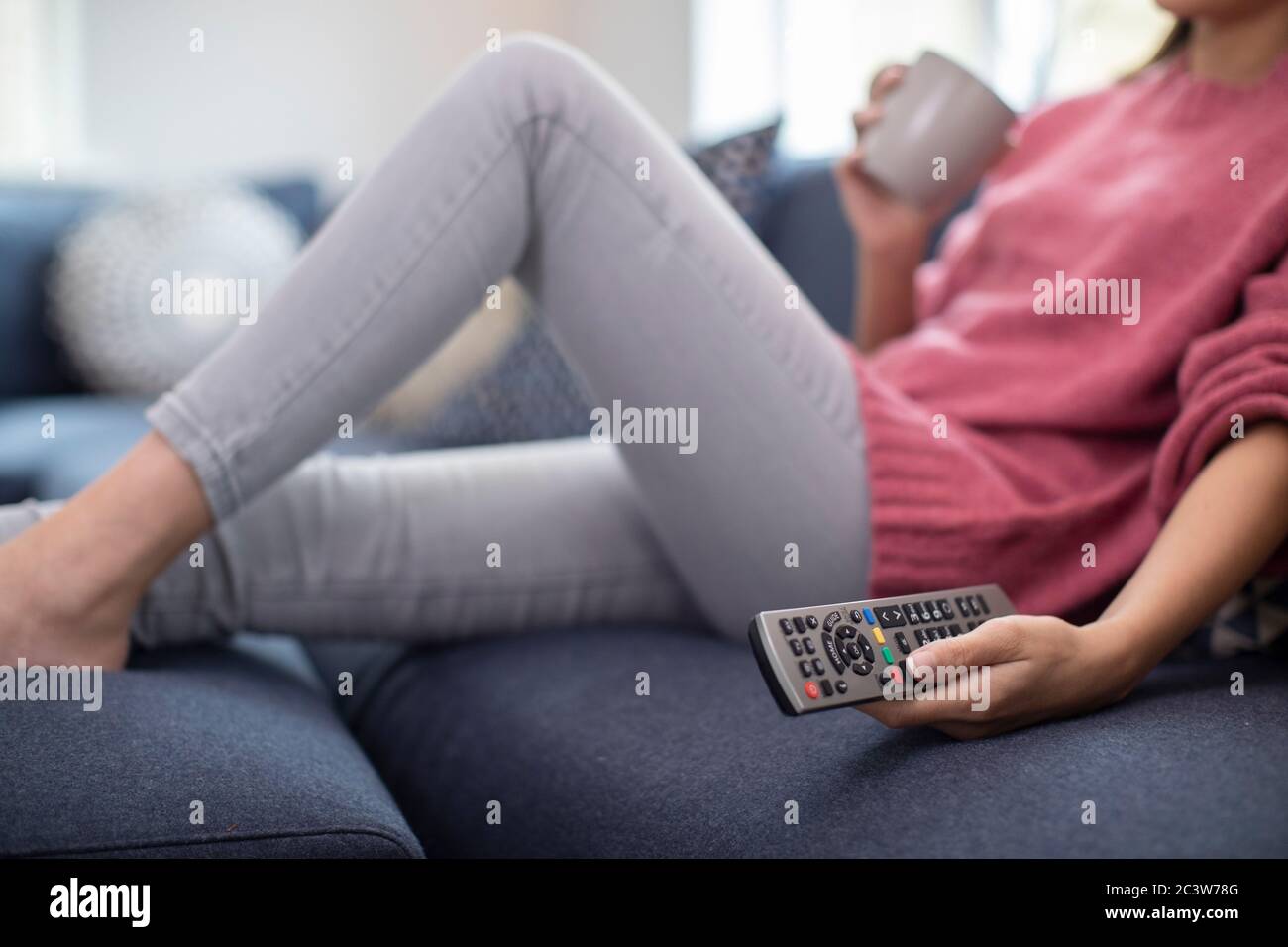 Dettaglio della donna rilassante sul divano tenendo premuto il telecomando e guardare la televisione Foto Stock