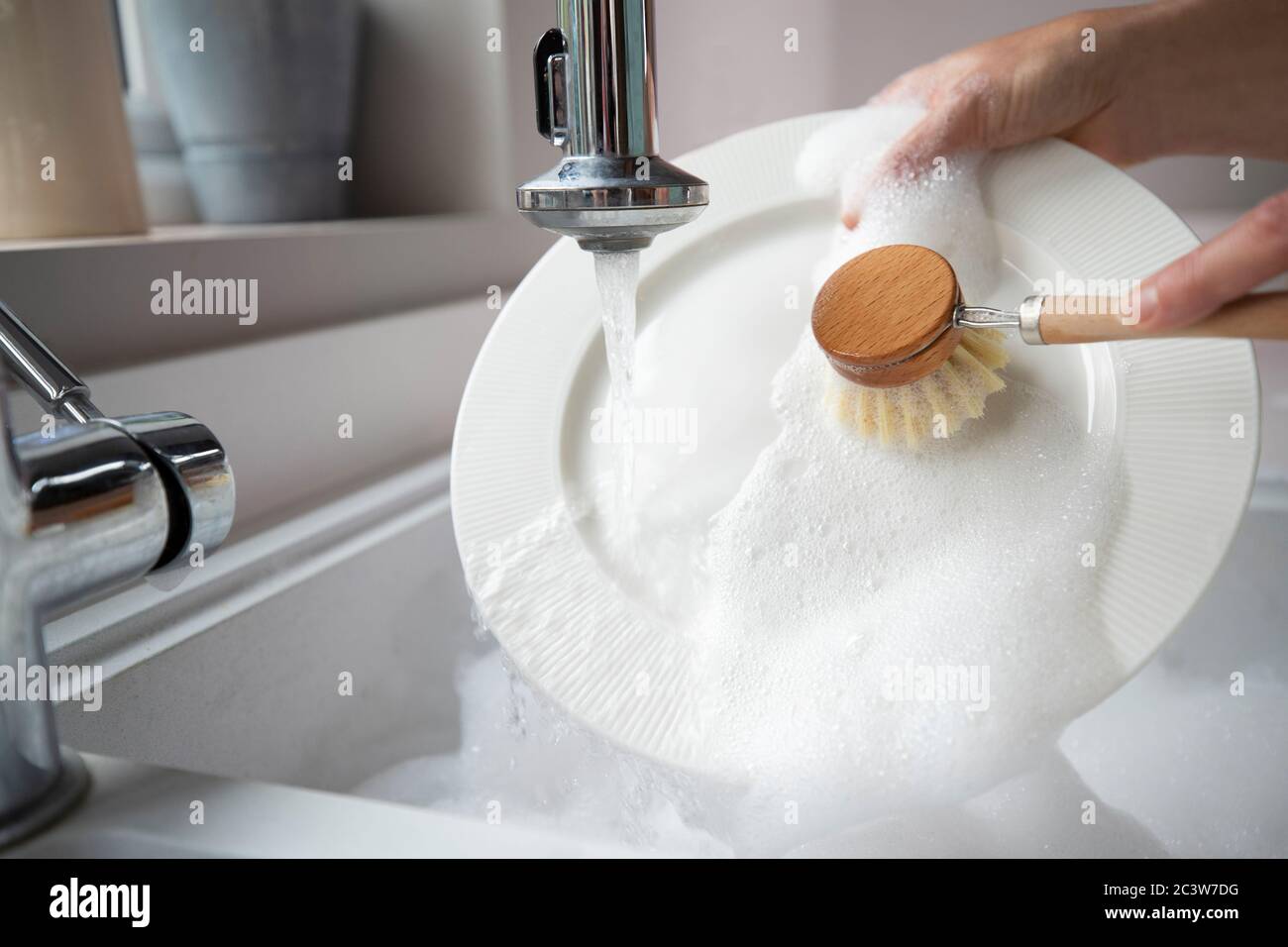 Donna lavaggio a casa utilizzando Eco Dish Brush per uno stile di vita sostenibile Foto Stock