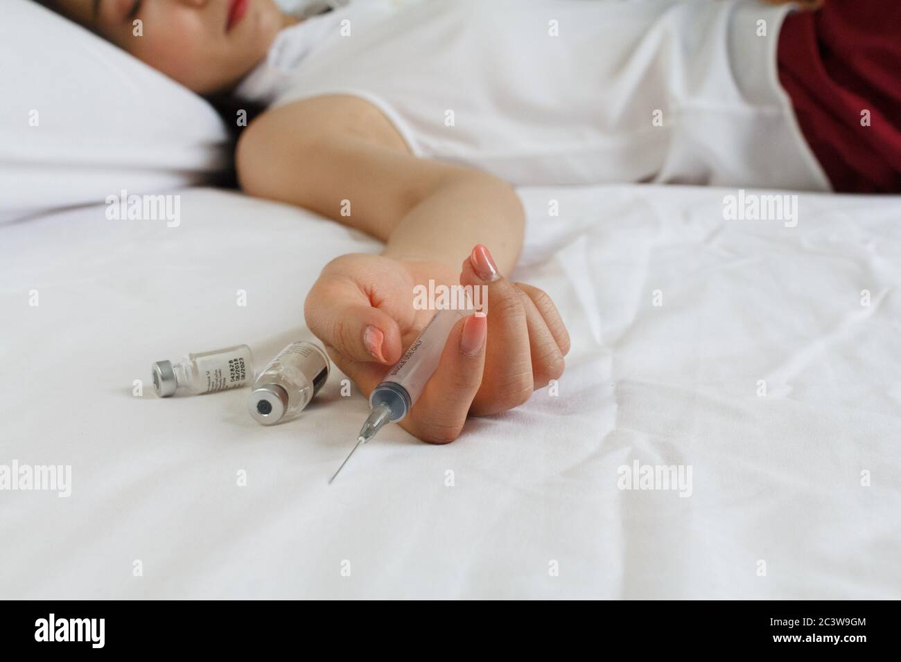 Concetto di droga - la donna è tossicodipendente per iniettare la mano passiva a letto. Pillole e iniezione Foto Stock