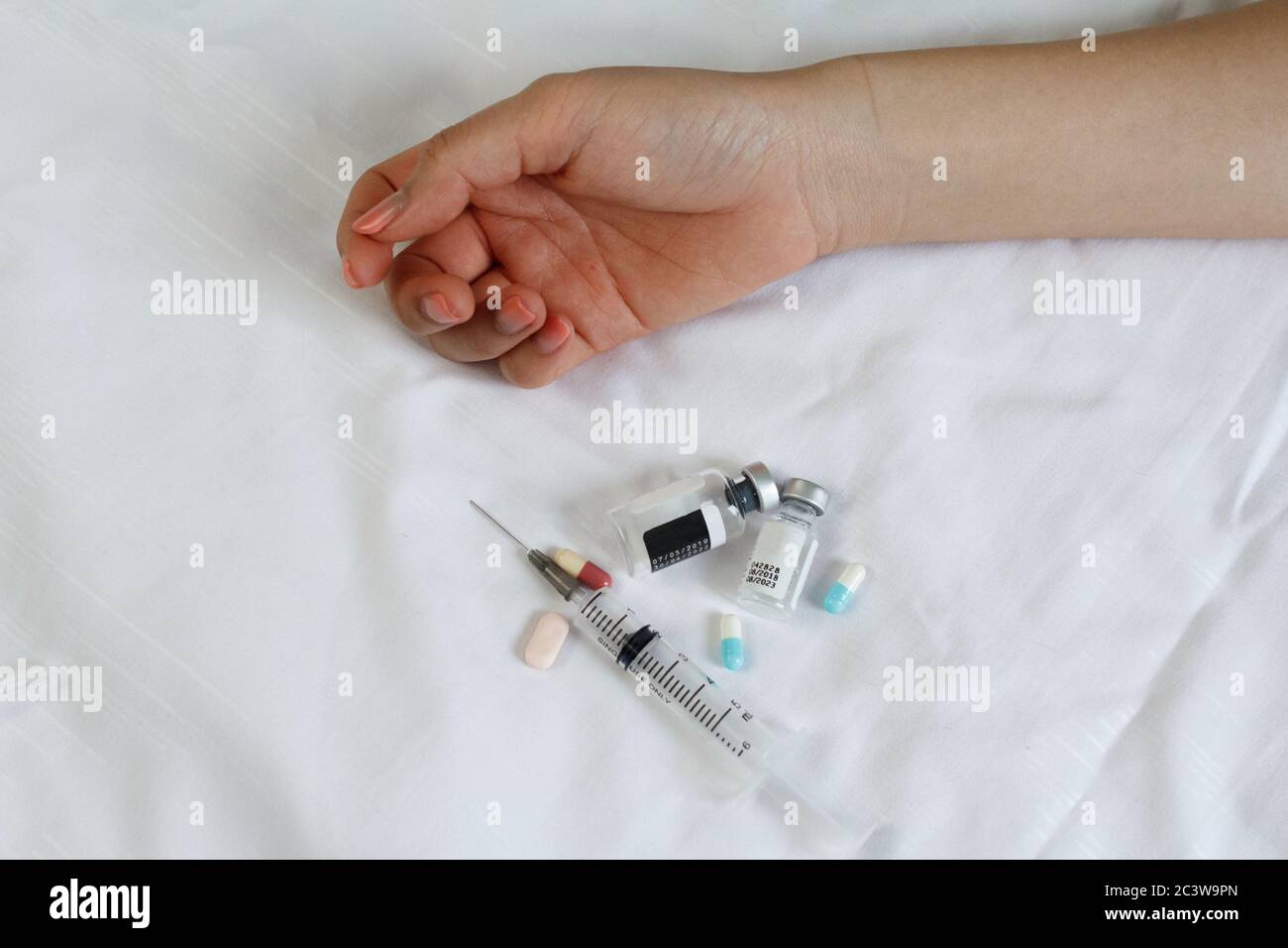 Concetto di droga - mano passiva sul letto. Pillole e iniezione Foto Stock