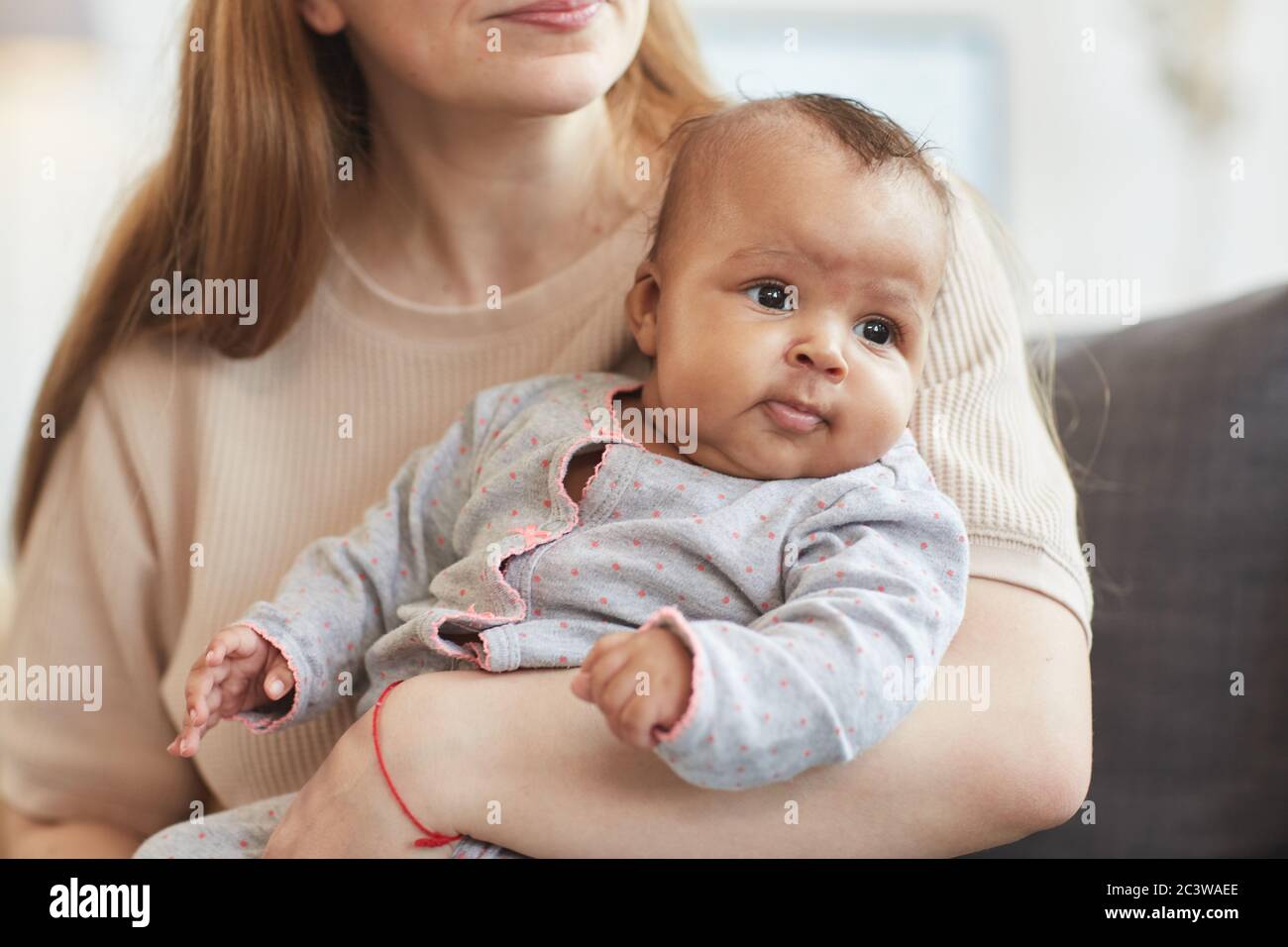 Ritratto di carino bambino misto corsa guardando via mentre si siede nelle mani di madre caucasica cura, spazio copia Foto Stock
