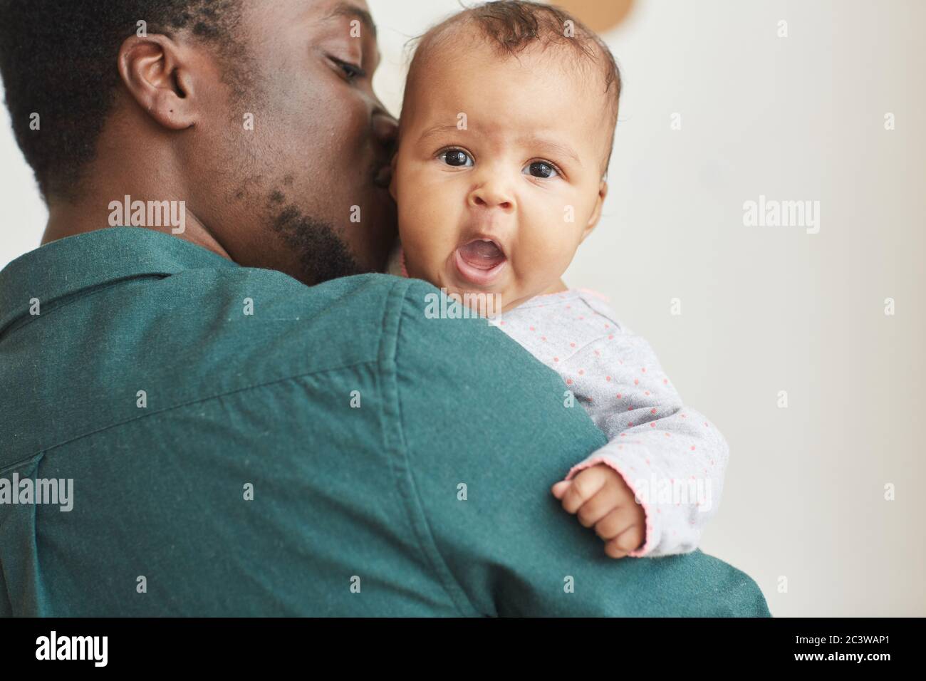 Indietro vista ritratto di giovane afroamericano padre che tiene il figlio con bambino carino guardando la fotocamera sopra la spalla mans, copia spazio Foto Stock