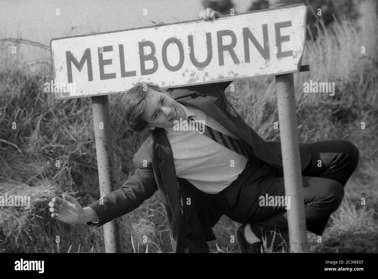 Anni ottanta, da Melbourne a ...bene Melbourne, sotto un cartello cittadino nello Yorkshire, Inghilterra, un'ondata da un giovane studente maschile che è fuori per vivere e iniziare una nuova vita in Australia e la città con lo stesso nome, Melbourne, Foto Stock