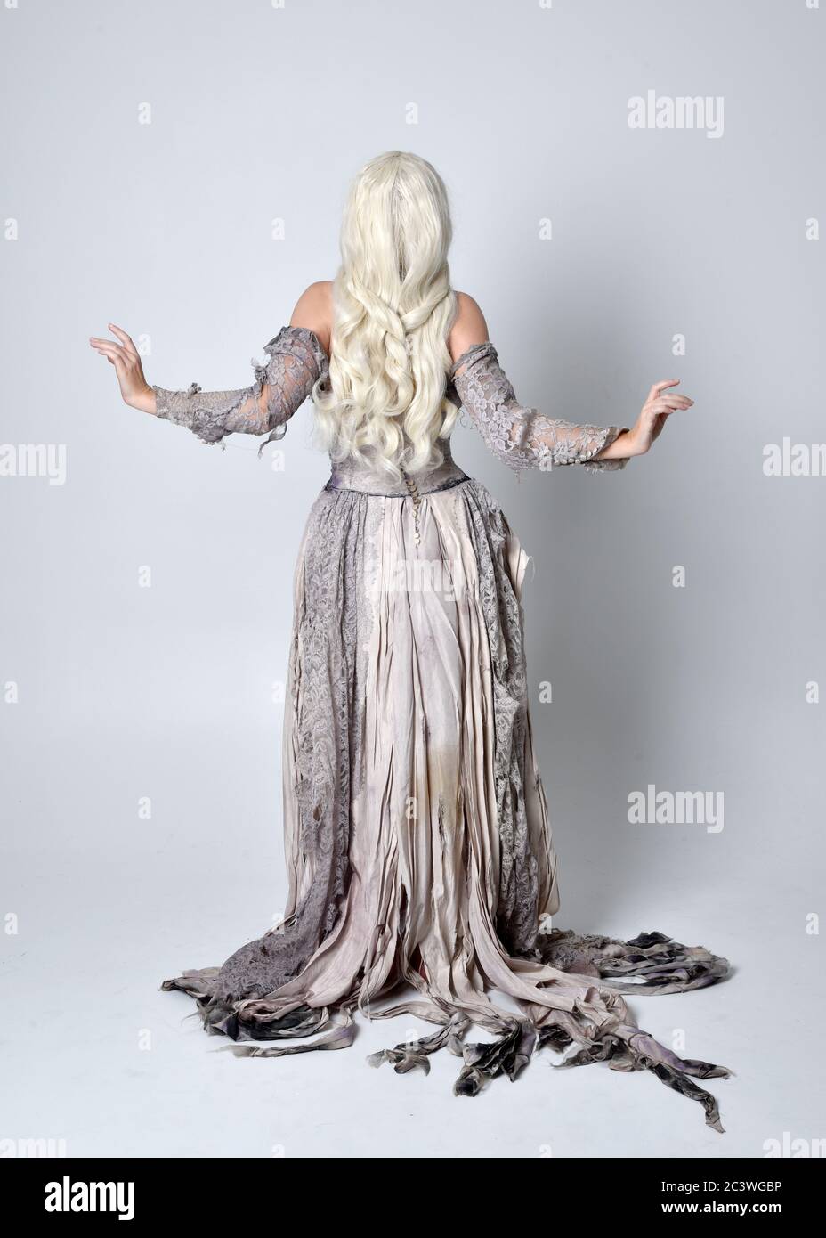 Ritratto di bionda ragazza che indossa strappato vecchio abito da sposa a lunghezza intera in piedi posa, isolato contro uno sfondo studio. Foto Stock