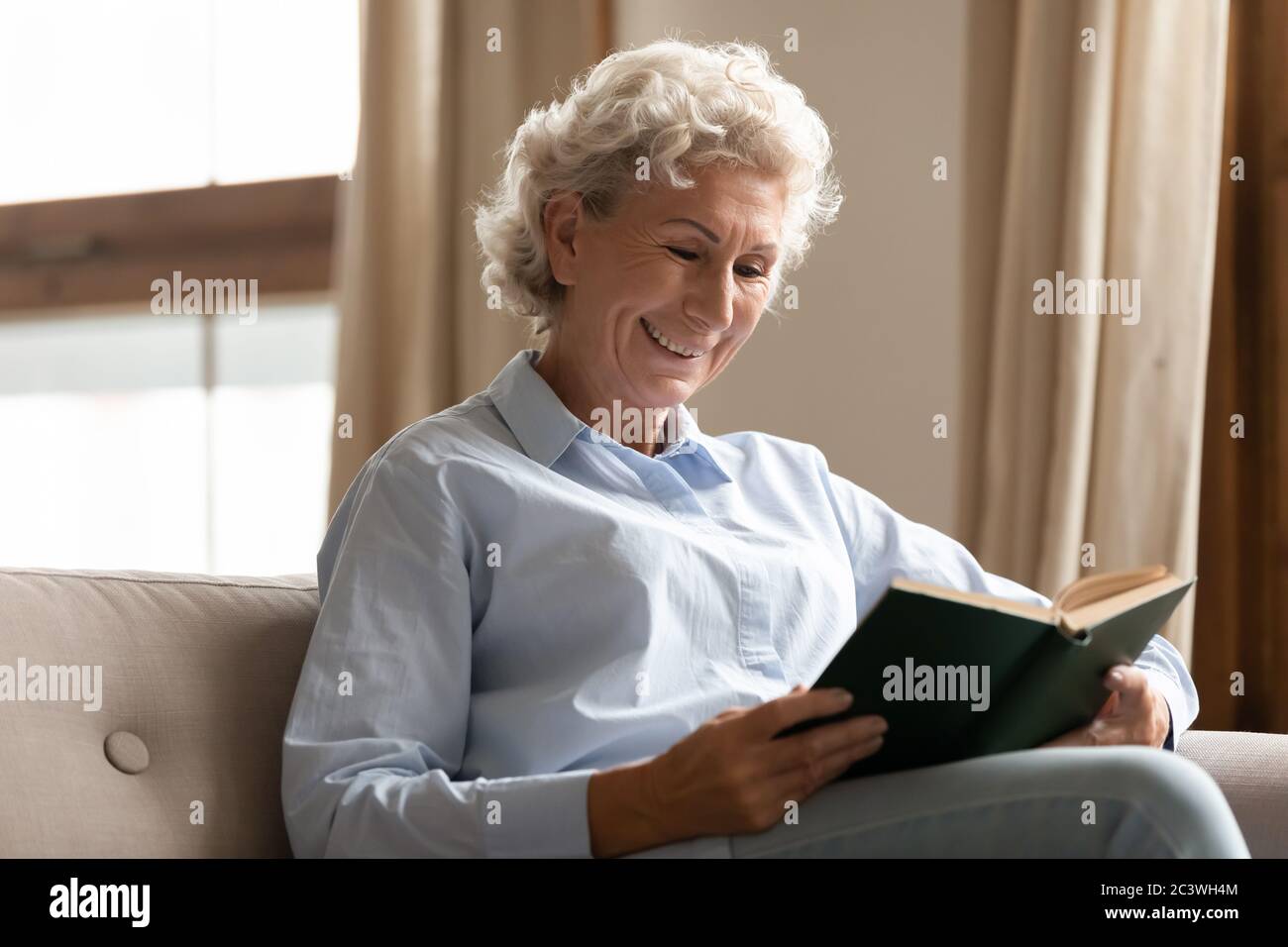Donna matura sorridente godere di tempo libero leggendo interessante libro Foto Stock
