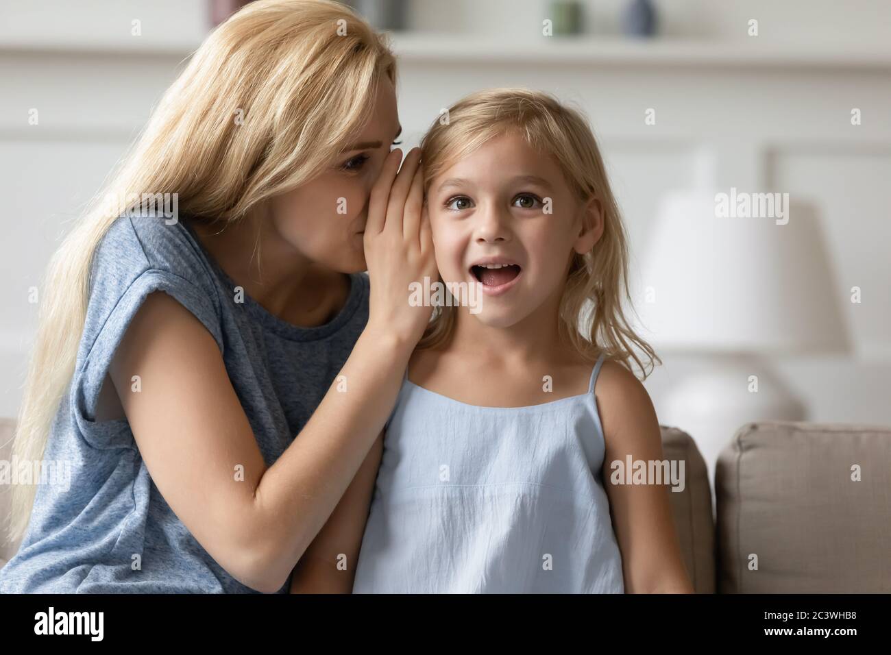 Madre sussurra sull'orecchio a figlia prescolare un segreto Foto Stock