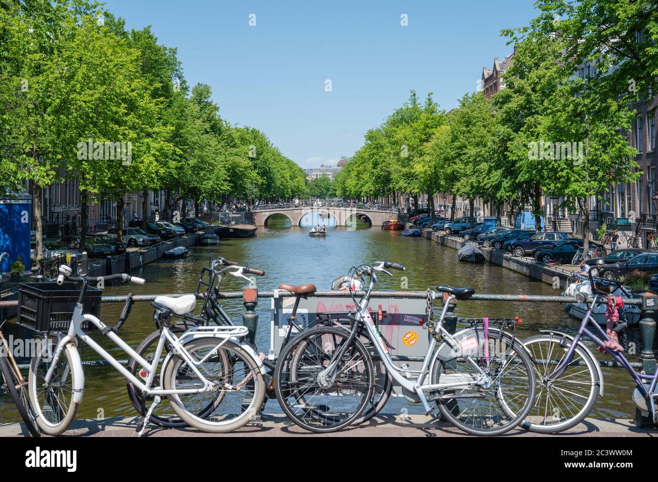 Canale Keizersgracht alberato nel centro di Amsterdam con biciclette parcheggiate contro la ringhiera e persone su una barca che naviga lungo il canale. Foto Stock