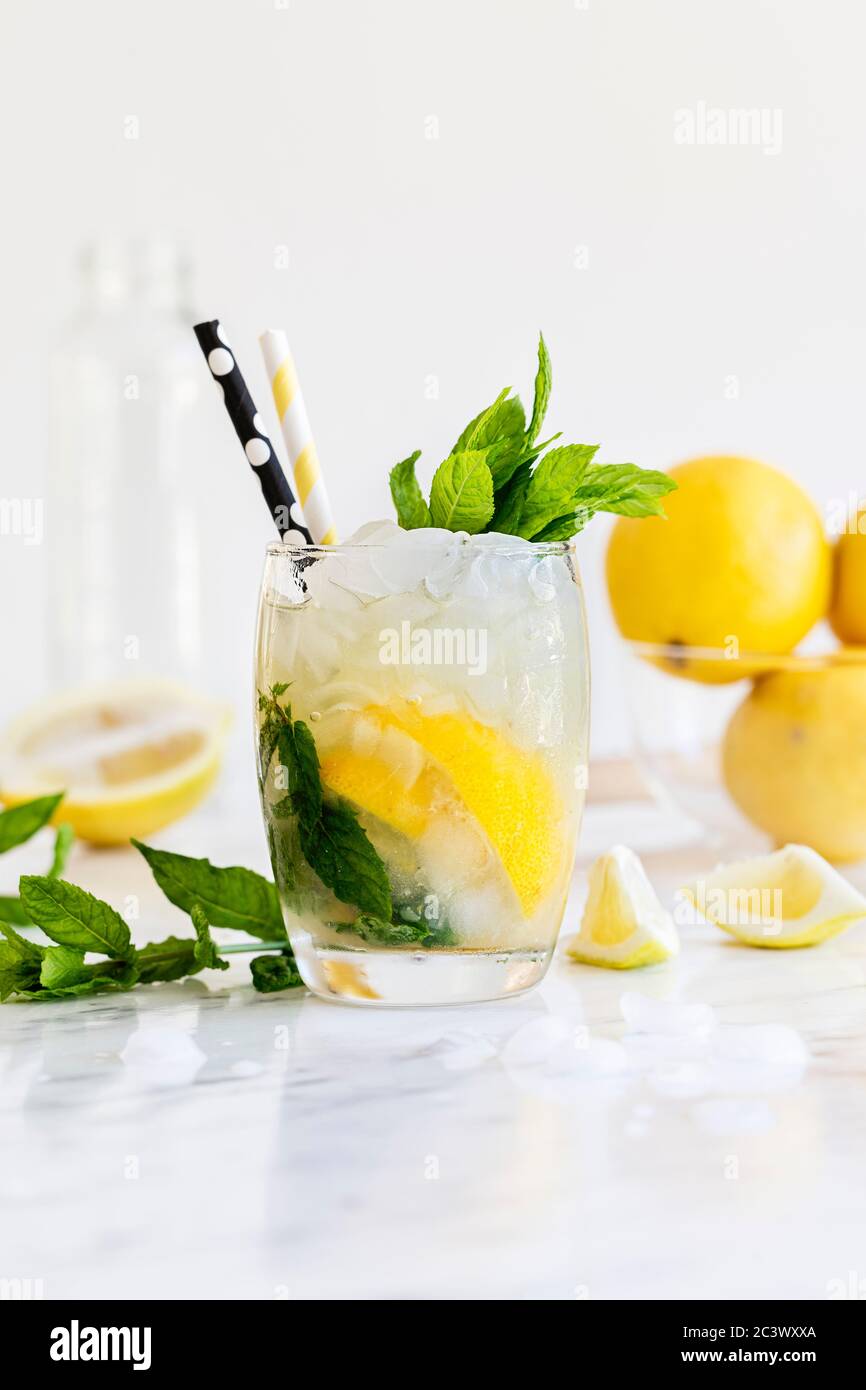 Una bevanda fresca di Mojito con foglie di menta, limone, lime e ghiaccio tritato. Su una superficie di marmo lucido, con limoni e menta sfocati sullo sfondo Foto Stock