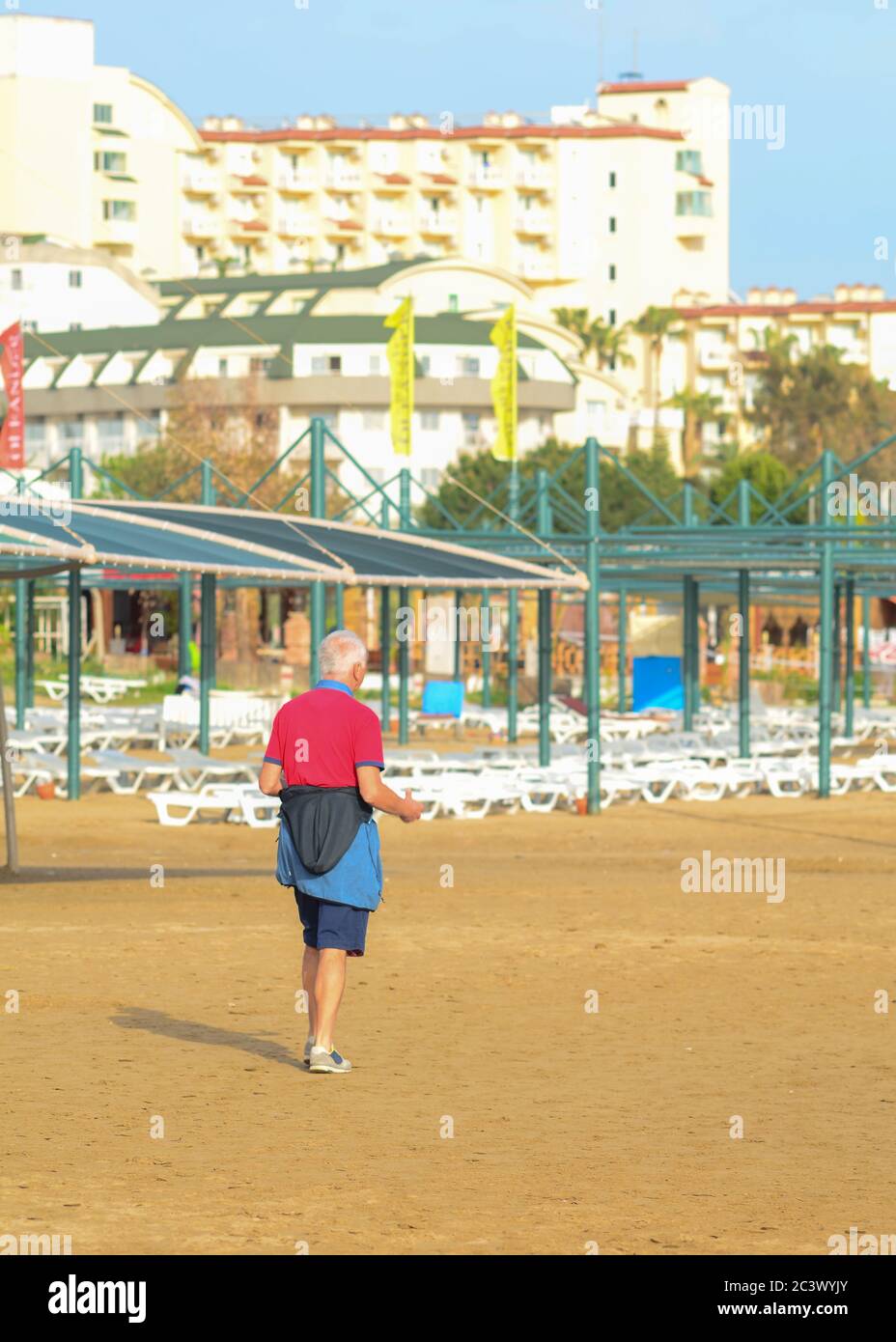 Side, Turchia - 12 aprile - 2019: Un uomo caucasico anziano in una T-shirt rossa e shorts sta facendo esercizi su una spiaggia vuota. La vista dal retro. Foto Stock