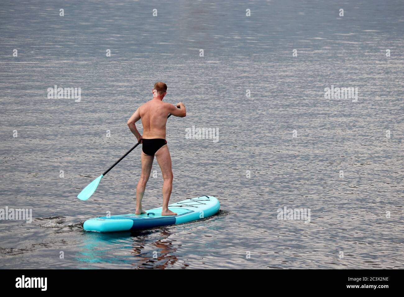 SUP surf, uomo in tronchi da nuoto in piedi con pagaia su una tavola in acqua. Paddle boarding in estate Foto Stock