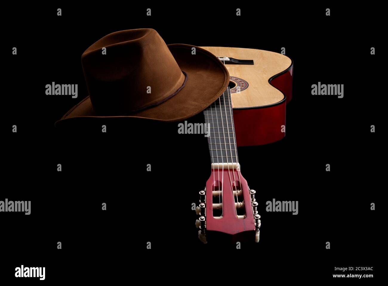 Cultura americana, canzone popolare e tema di concetto muisc paese con un cappello cowboy e una chitarra acustica isolato su sfondo nero con luci drammatiche Foto Stock