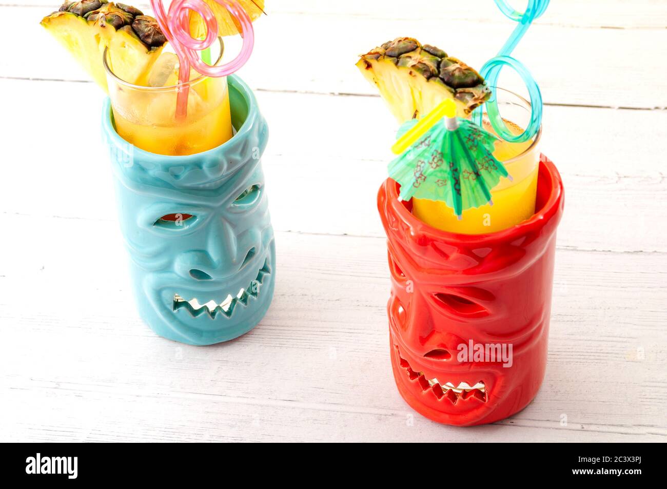 Bar Hawaiiano, vacanza estiva e tema di concetto di bevande da spiaggia con tazze Tiki su tavolo di legno bianco con ogni tazza che ha una paglia di plastica, un cocktail umbre Foto Stock