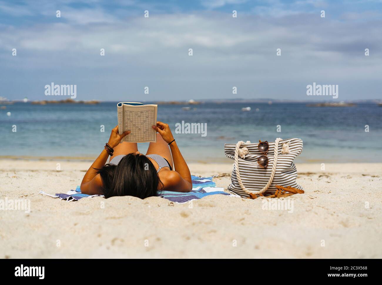 Donna abbronzata che legge e si gode sulla spiaggia vicino all'oceano Foto Stock