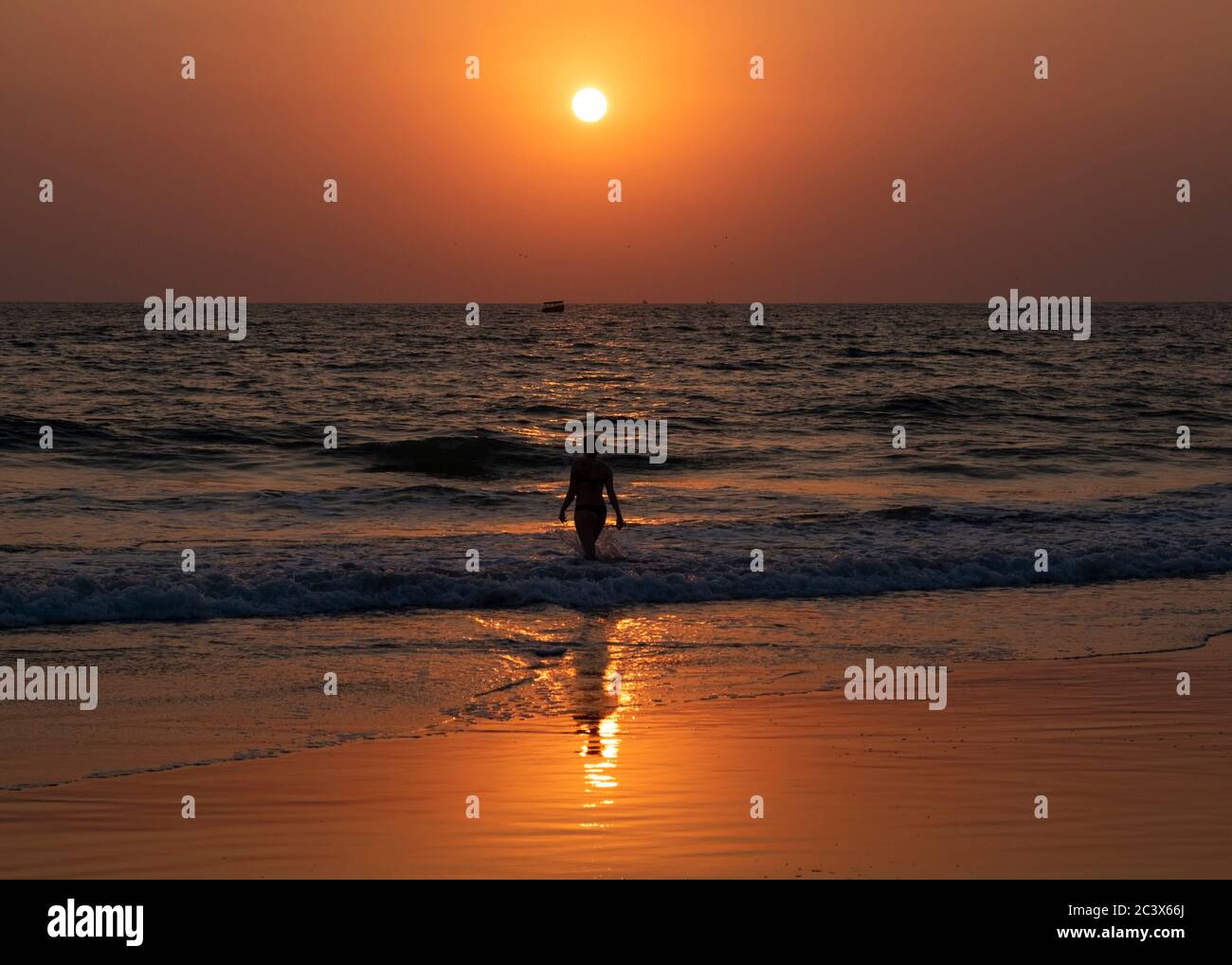 Silhouette di una giovane donna al tramonto in acqua a Majorda spiaggia a Goa, India Foto Stock