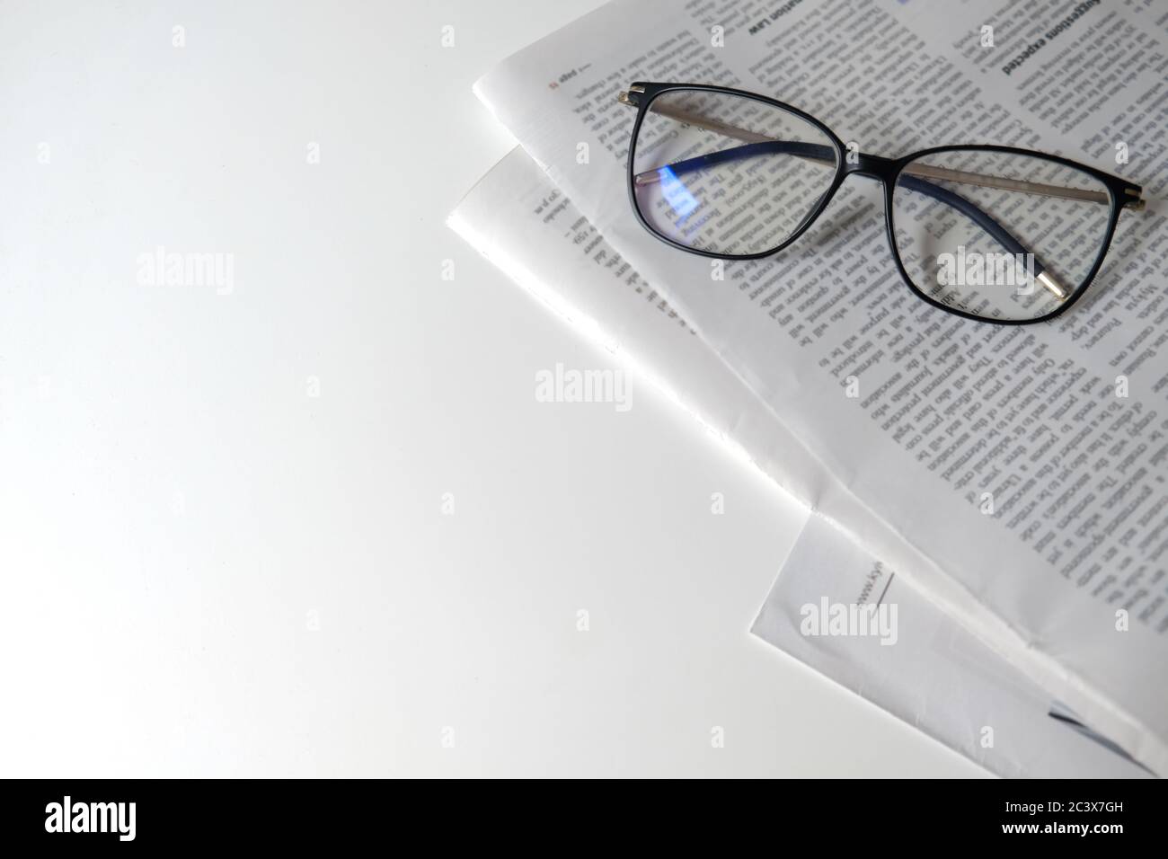 Leggere il giornale in isolamento. Luogo di apprendimento per la casa o il luogo di lavoro per un freelance. Giornale e occhiali su una scrivania bianca, spazio vuoto Foto Stock