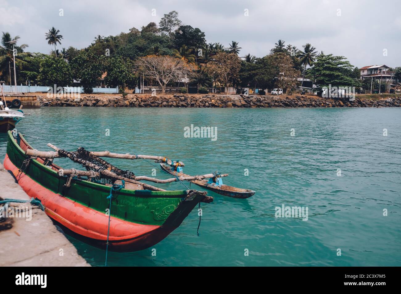 Colorata vernice rossa e verde barca da pesca legata alla riva. Vista panoramica dal molo. Artigianato locale in Sri Lanka. Acqua di mare blu. Foto Stock