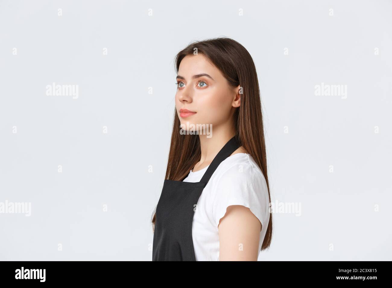 Dipendenti, lavoro, piccole imprese e concetto di caffetteria. Barista carino sognante in grembiule nero, operaio di caffè guardando a sinistra con premuroso Foto Stock