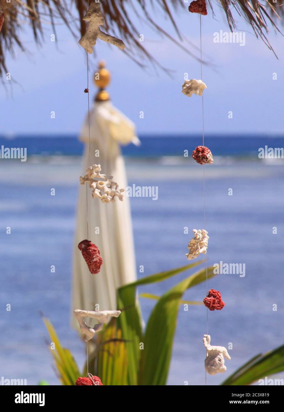 Decorazioni in corallo rosso e bianco, appesi su filo all'esotico bar sulla spiaggia, con ombrello sfocato e onde marine sullo sfondo, su Gili Air isl Foto Stock