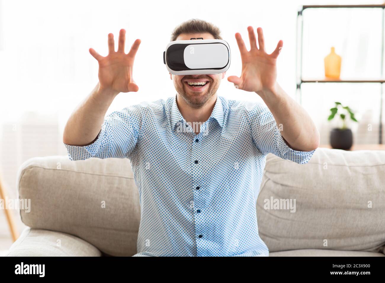 Giovane uomo che indossa occhiali per realtà virtuale, seduto sul divano Foto Stock