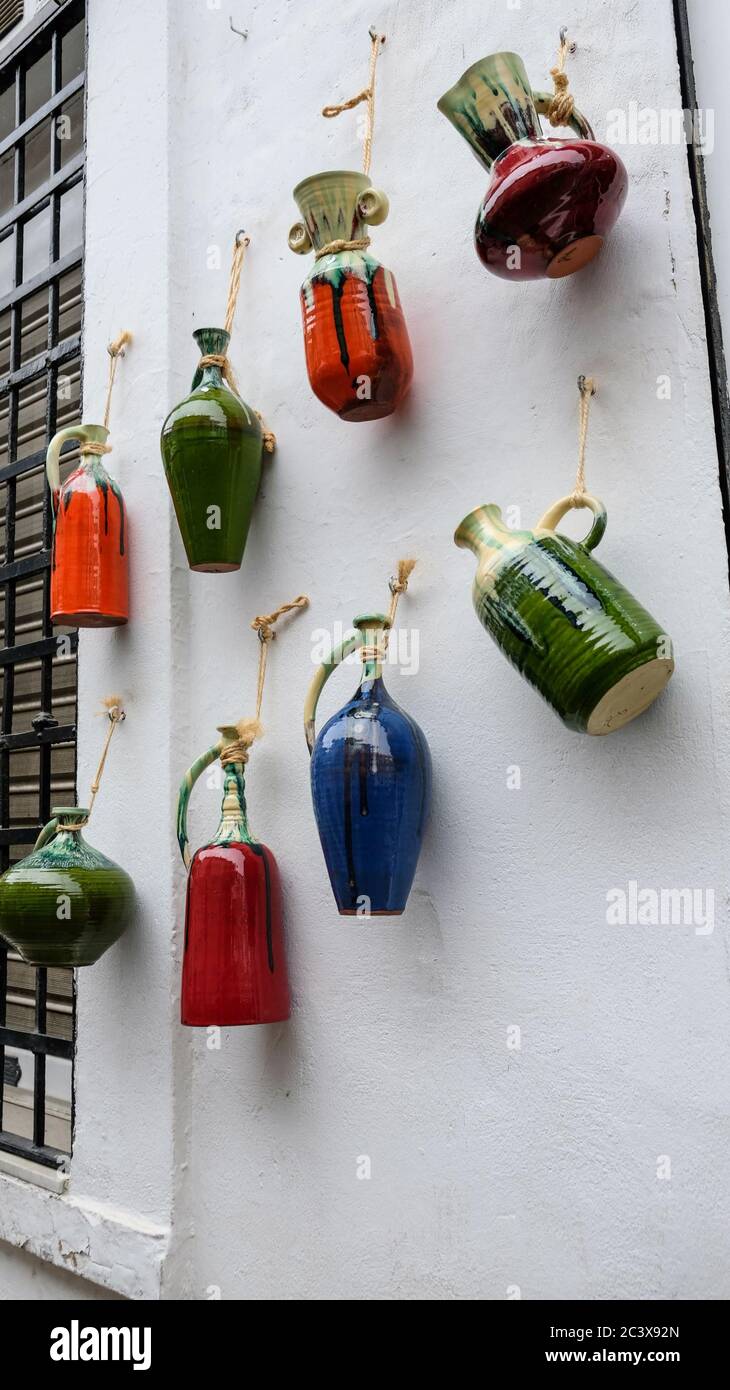 Cordoba / Spagna - 2019: Bottiglie e brocche colorate in ceramica dipinte di terra appese su una parete bianca all'esterno del negozio di souvenir. Creta che crafting Foto Stock