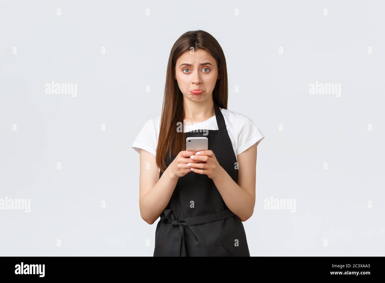 Dipendenti di negozi di alimentari, piccole aziende e caffè concetto. Sconvolto e deluso pouting carina barista femminile, lavoratore in caffè che tiene mobile Foto Stock