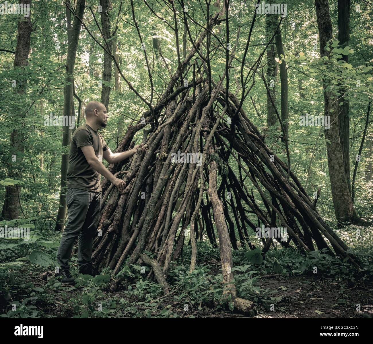 Uomo che costruisce un rifugio di sopravvivenza nella foresta. Rifugio nei boschi da rami di alberi. Foto Stock