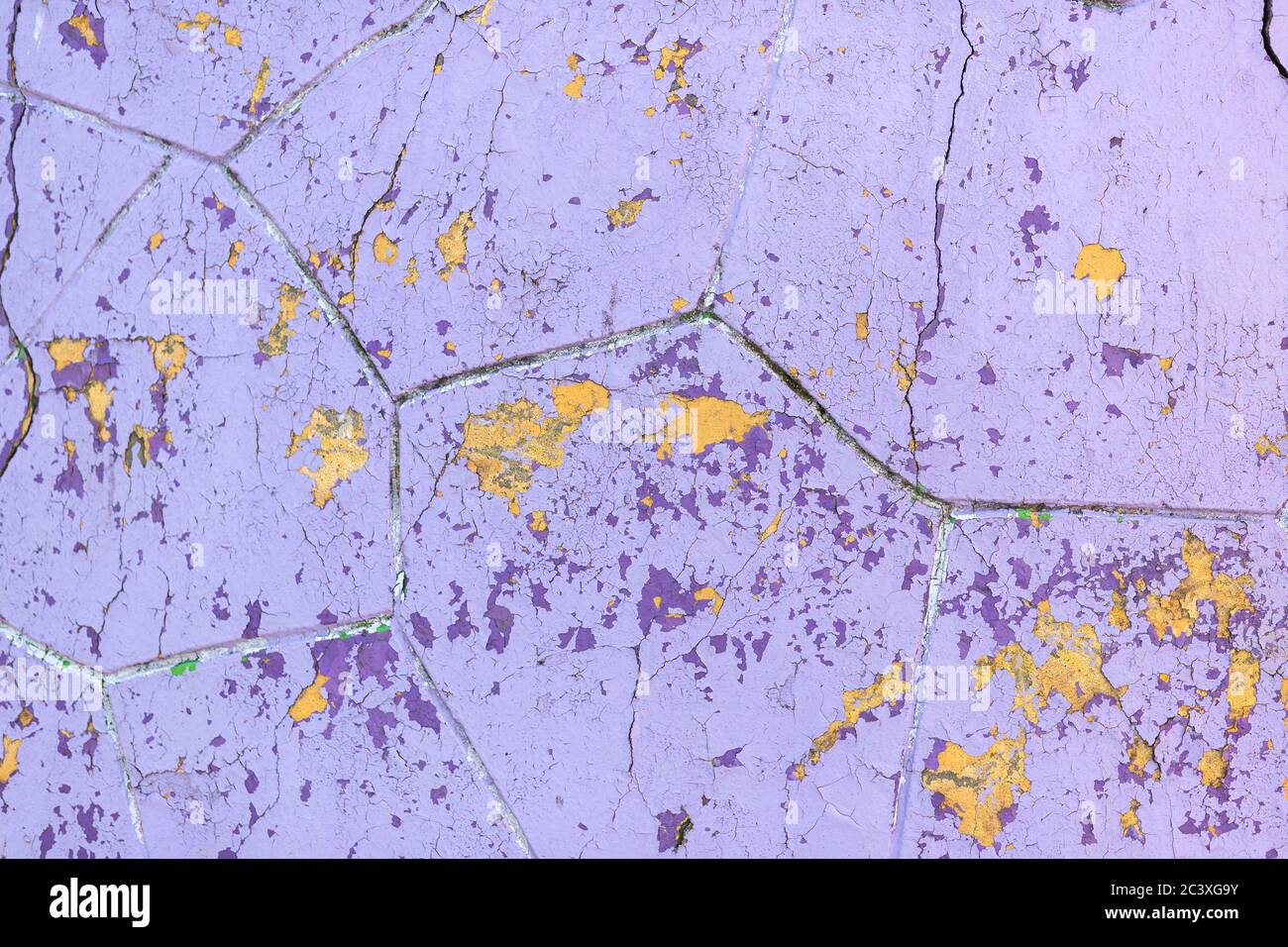 Sfaldatura di vernice viola e gialla sulla vecchia superficie della parete. Facciata dell'edificio con vernice danneggiata. Sfondo astratto, primo piano, texture. Foto Stock