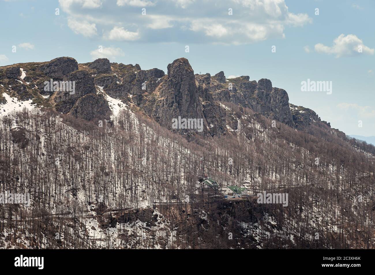 Impressionanti, puntinose, colonne rocciose di montagna, alberi senza foglie, neve rimanente sul terreno e cielo blu con nuvole bianche Foto Stock