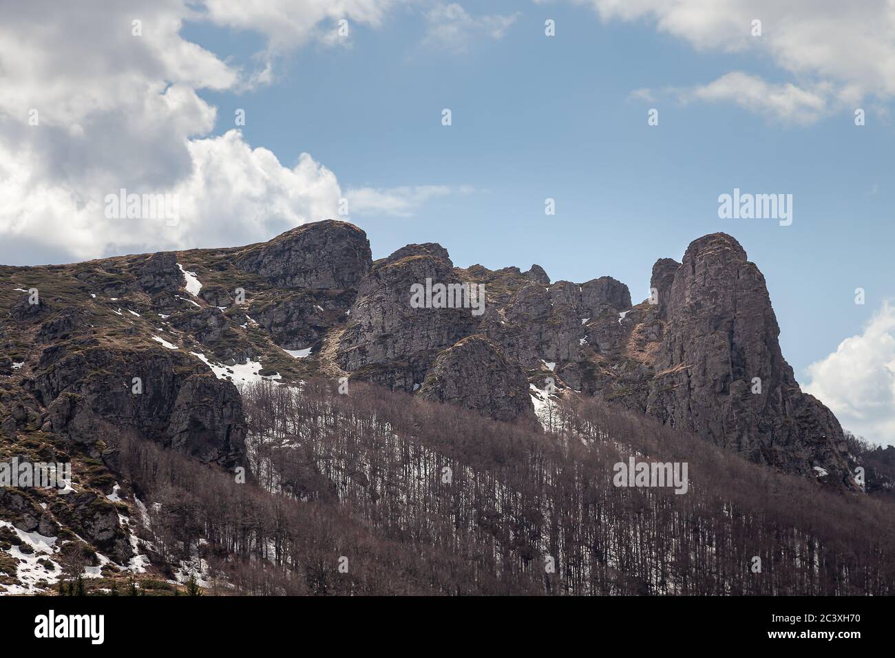 Impressionanti, puntinose, colonne rocciose di montagna, alberi senza foglie, neve rimanente sul terreno e cielo blu con nuvole bianche Foto Stock