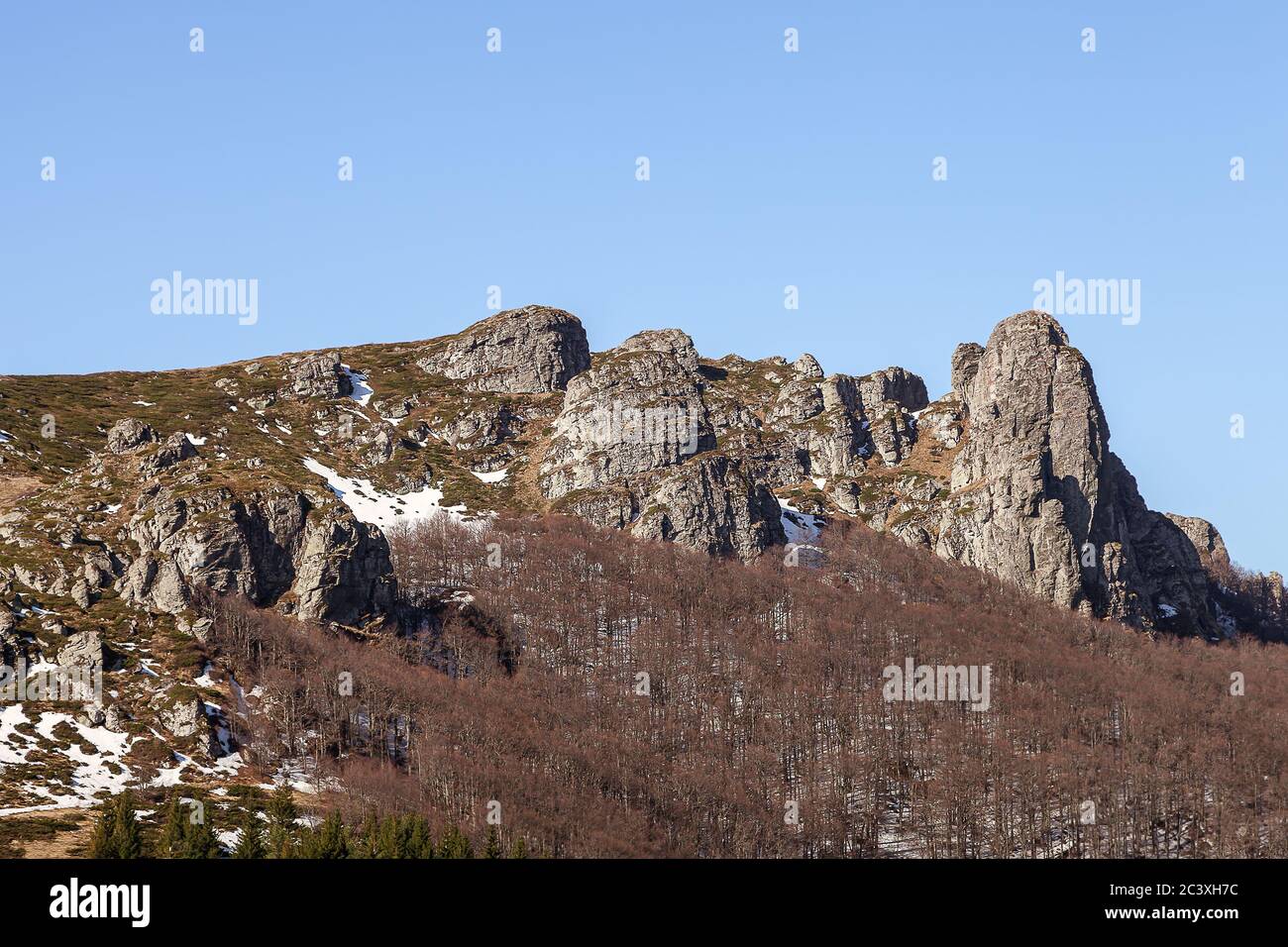 Impressionanti, puntinose, colonne rocciose di montagna, alberi senza foglie, neve rimanente sul terreno e cielo blu con nuvole bianche Foto Stock