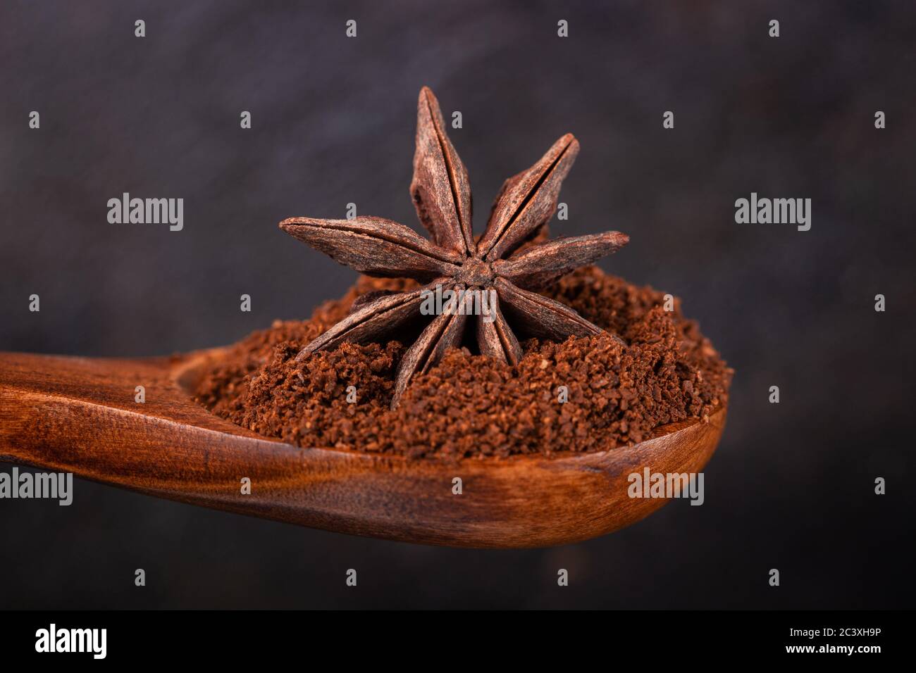 Anice stellato in un cucchiaio di legno con caffè macinato su sfondo scuro Foto Stock