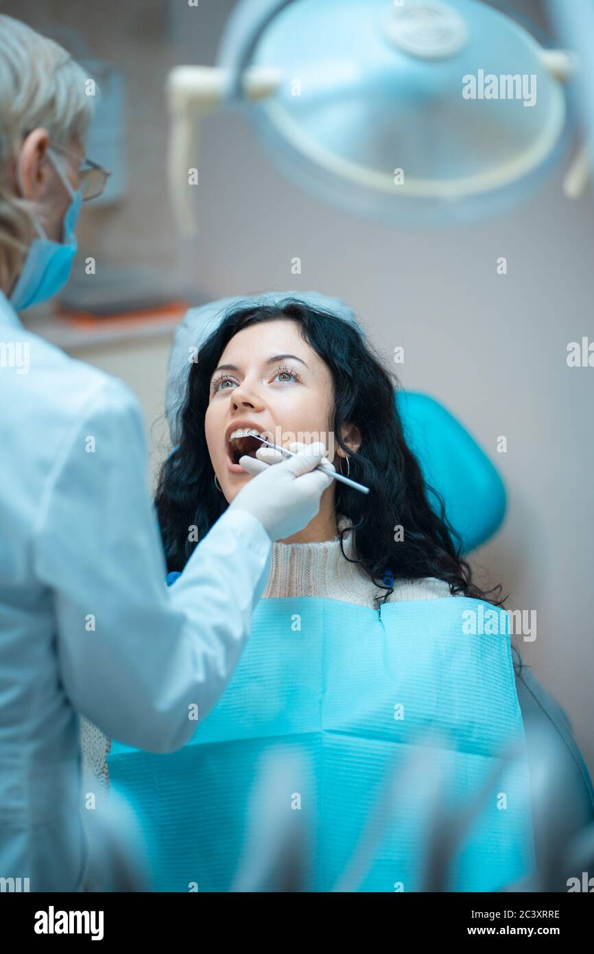 bella brunette curly donna dentista trattare paziente in clinica moderna Foto Stock