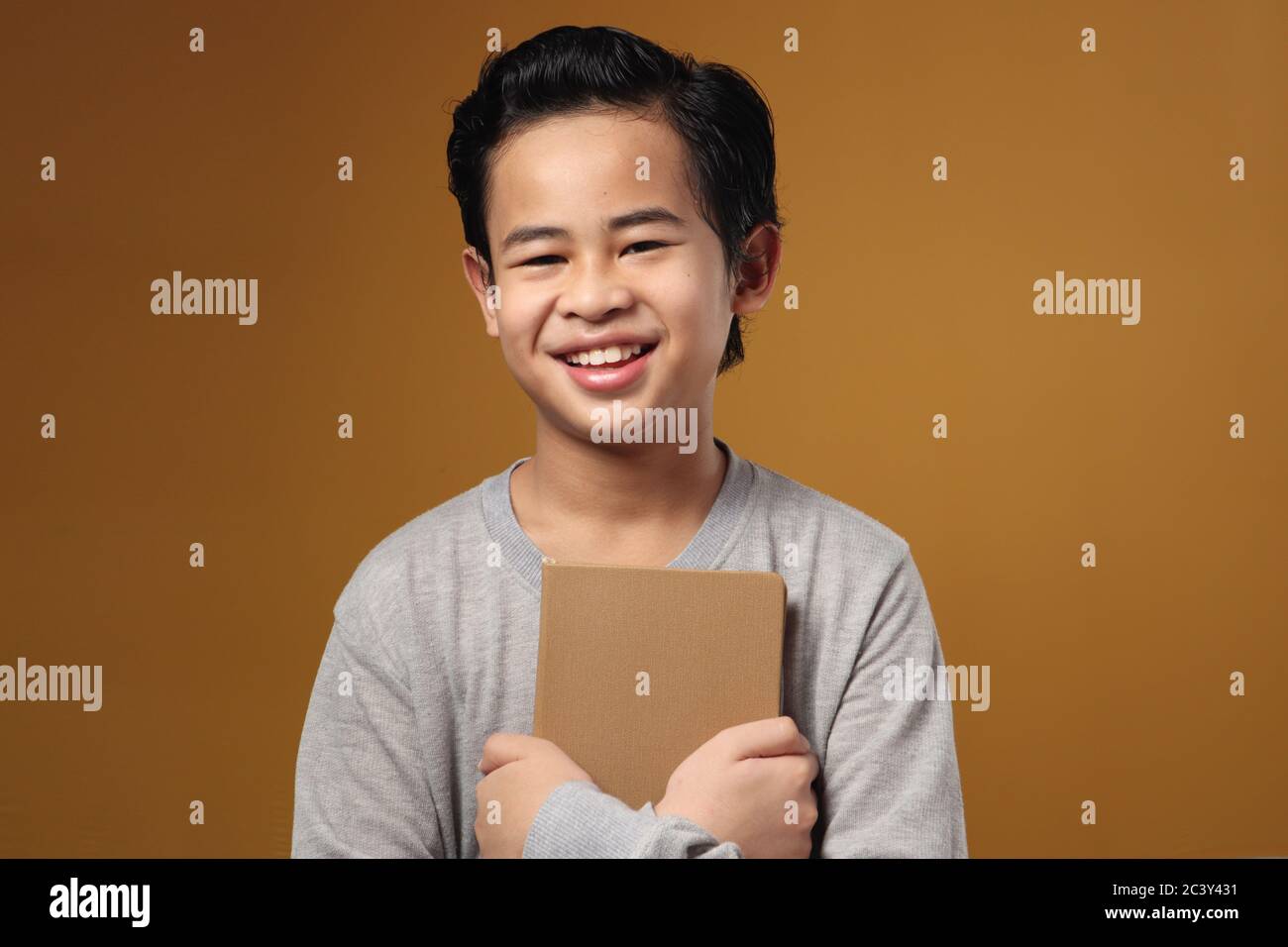 Ritratto di studente asiatico che tiene libro e sorridendo alla macchina fotografica, scolaro intelligente, su sfondo giallo Foto Stock