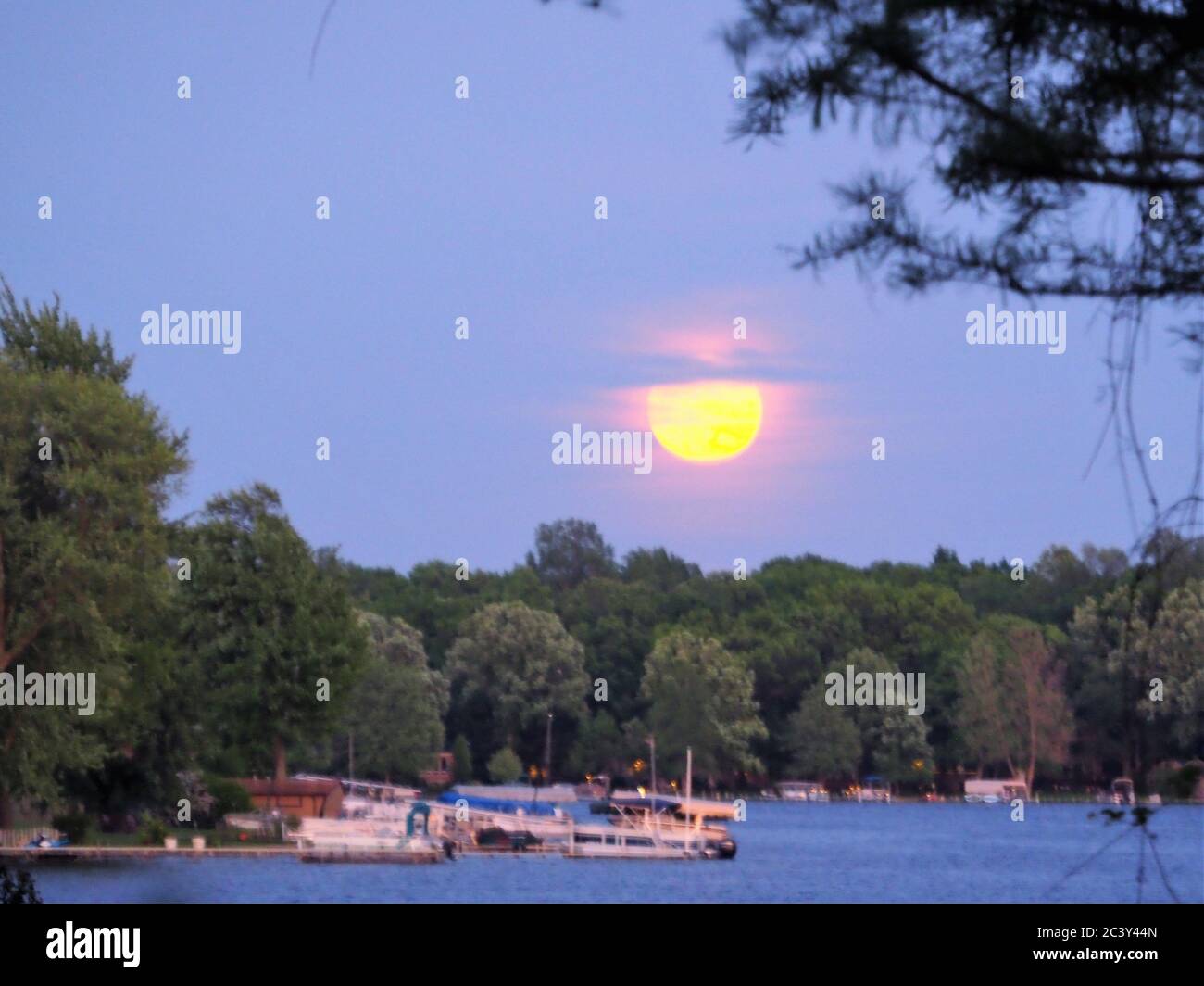 Luna Rising attraverso le nuvole rosa sopra un lago Foto Stock