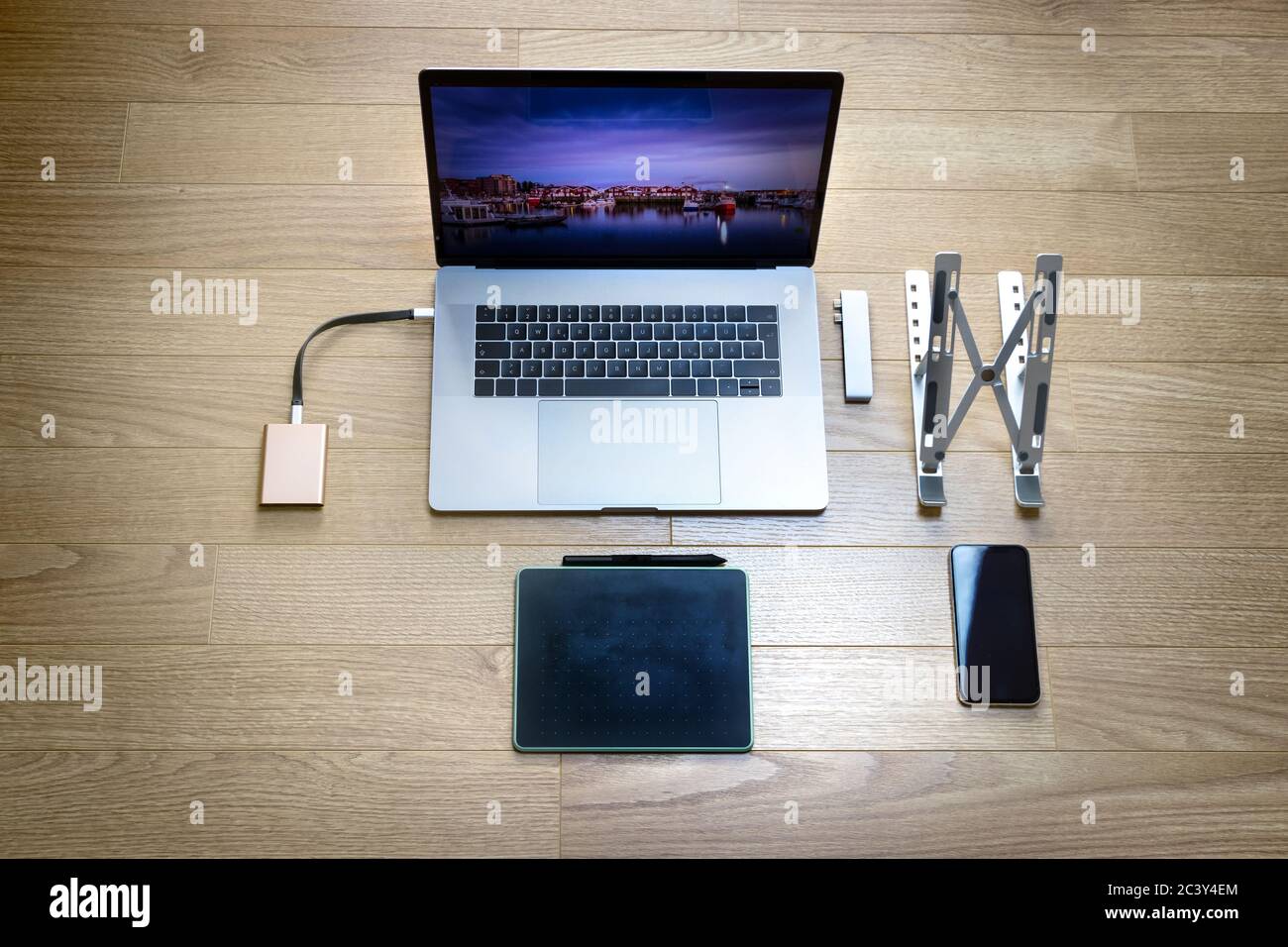 Vista dall'alto di un notebook con un tablet grafico, un telefono cellulare, un supporto pieghevole, un disco rigido ssd e un adattatore hub di tipo C. Foto Stock