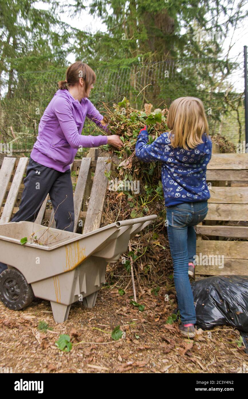 Donna e figlia di 10 anni gettando piante di fragola assottigliate sul palo di composto in Issaquah, Washington, Stati Uniti Foto Stock