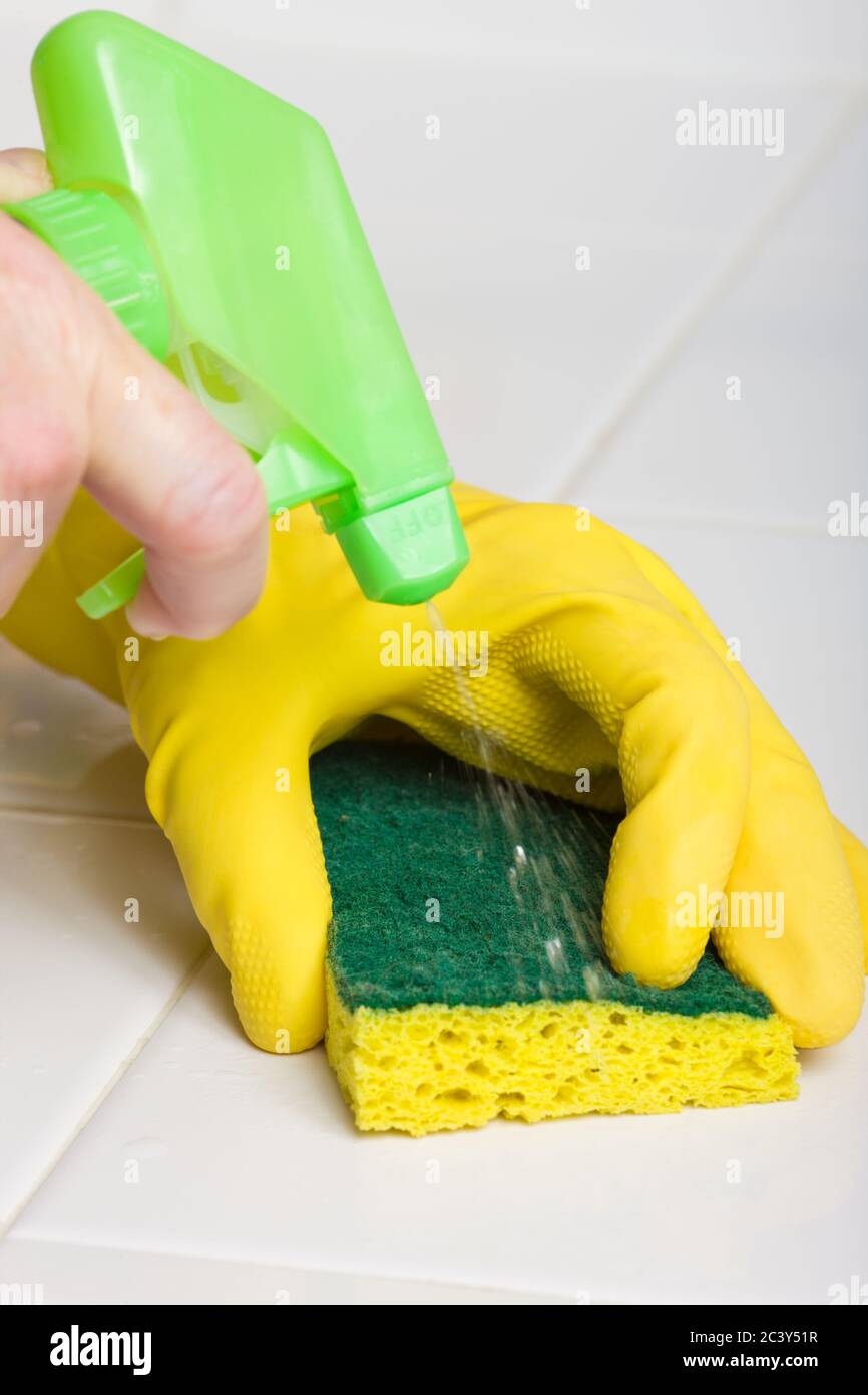 Donna che indossa un guanto di gomma gialla che lava un piano di lavoro con una spugna e uno spray che esce da una bottiglia di pulizia Foto Stock