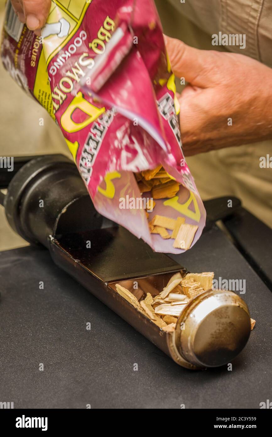 Uomo che versa i trucioli di alderwood in un vassoio di trucioli di legno di un fumatore elettrico da 30'. I trucioli di legno fumatore aiutano a infondere la carne o il pesce che fumano con sapori Foto Stock