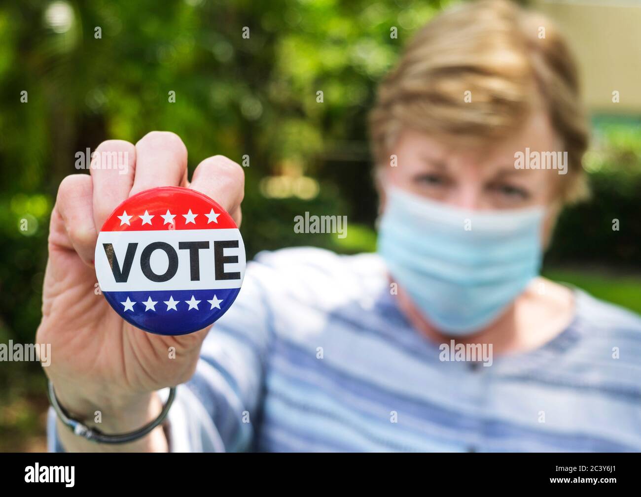 Ritratto di donna che indossa una maschera chirurgica tenendo premuto il pulsante di voto Foto Stock