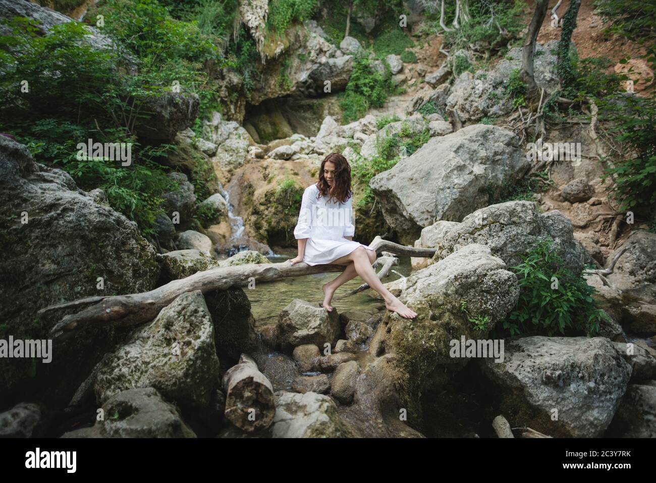 Ucraina, Crimea, giovane donna seduta sul ramo sopra il fiume nel canyon Foto Stock