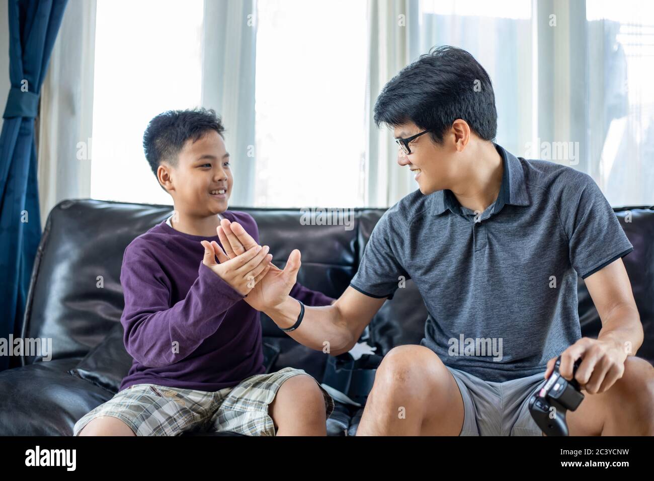 Padre e figlio asiatici si divertono a giocare con i videogiochi insieme al joystick video con eccitare e molto divertimento nel soggiorno a casa Foto Stock