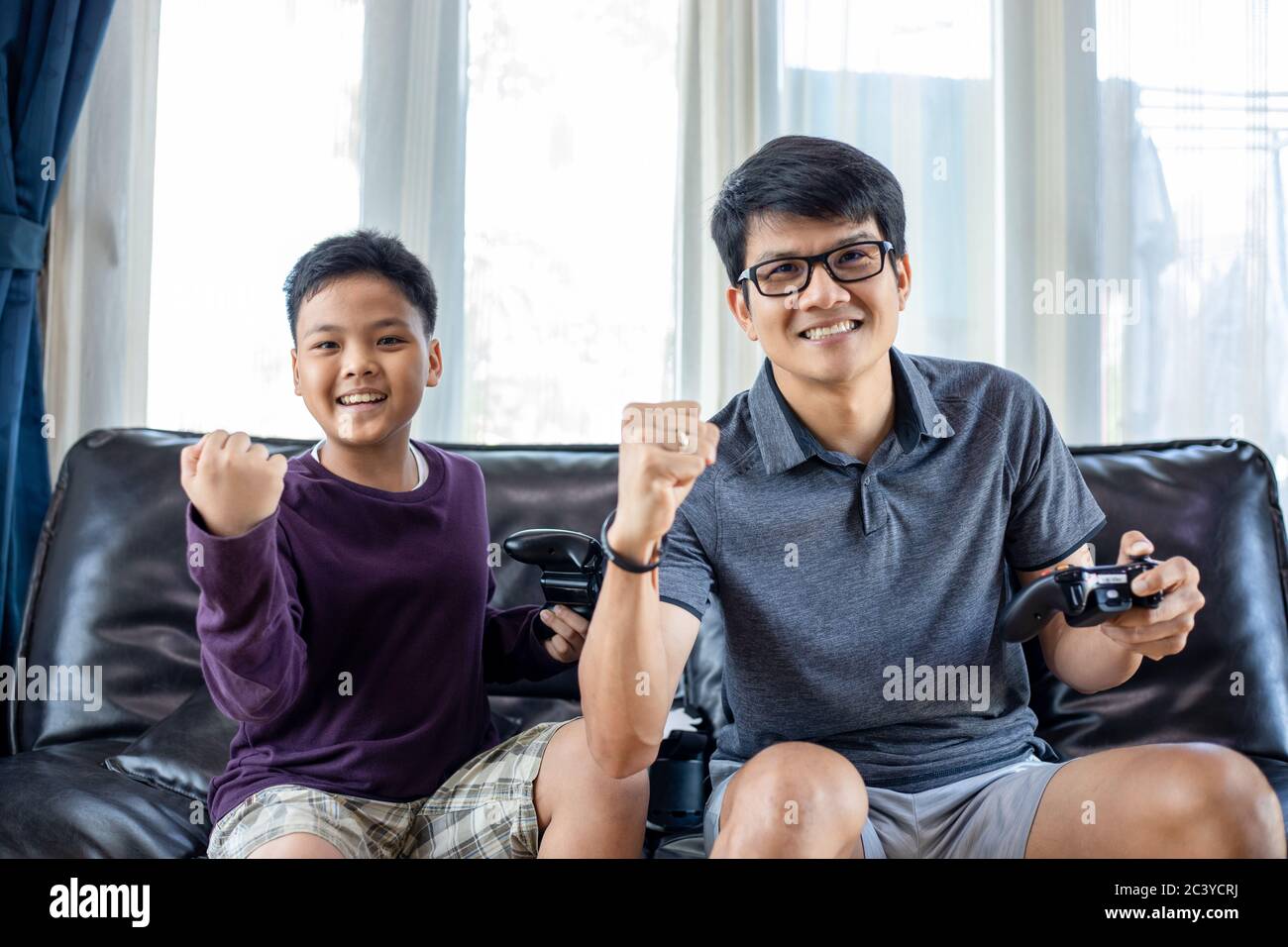 Padre e figlio asiatici si divertono a giocare con i videogiochi insieme al joystick video con eccitare e molto divertimento nel soggiorno a casa Foto Stock